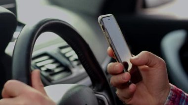 Direksiyon başında oturan ve akıllı bir telefonun ekranında kayan bir adamın görüntüsü. Bir adam arabada otururken akıllı telefon kullanır. Yüksek kalite 4k görüntü