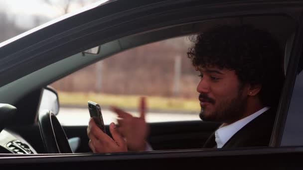 Młody Kręcony Facet Siedzi Samochodzie Patrzy Coś Przez Telefon Młody — Wideo stockowe