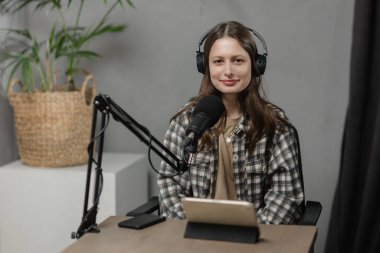 Mikrofonlu güzel kız podcast 'e katılıyor. Kareli gömlekli ve kulaklıklı genç bir kadın kameraya bakıyor. Yüksek kalite fotoğraf