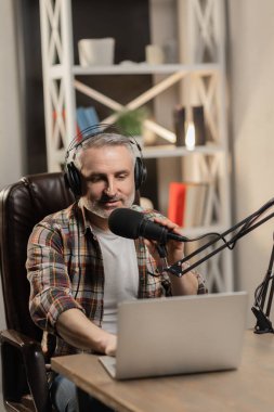 Kareli gömlekli adam podcast sunuyor. Profesyonel mikrofon ve kulaklıkla blogger yayın yapıyor. Yüksek kalite fotoğraf