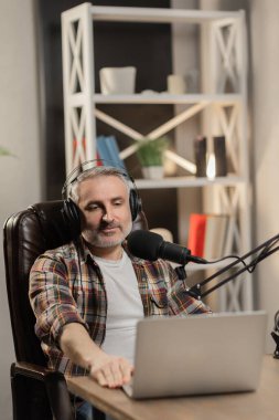 Kareli gömlekli tele-işçi odasında podcast yapıyor. Profesyonel mikrofonu ve kulaklığı olan son sınıf öğrencisi yayın yapıyor. Yüksek kalite fotoğraf