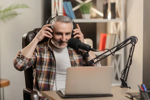 stock image Senior man is putting on headphones to do a podcast. Blogger recording video with professional microphone. High quality photo