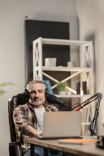 stock image Focused man in headphones and checkered shirt is doing podcast. Teleworker recording video with professional microphone. High quality photo