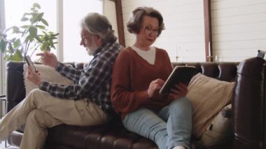 Gözlüklü yaşlı çift boş zamanlarında akıllı telefon ve dijital tablet kullanıyor. Gülümseyen kıdemli adam ve kadın aletler kullanıyor. Yüksek kalite 4k görüntü