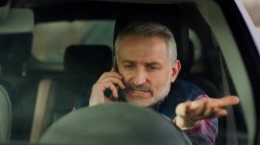Gri saçlı ve sakallı bir adam arabada oturur ve telefonda konuşur. Orta yaşlı bir adam bir arabanın direksiyonunda oturur ve telefonla elinde hareketlerle konuşur. Yüksek kalite 4k görüntü