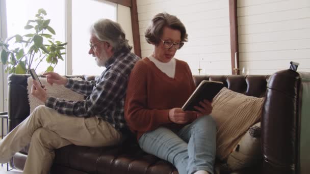 Pareja Jubilada Usando Smartphone Tableta Digital Mientras Está Sentada Sofá — Vídeos de Stock