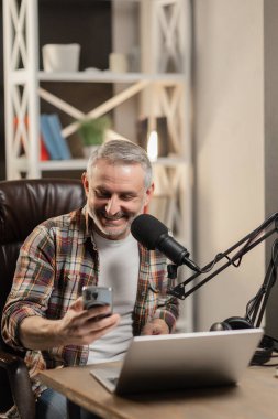 Gülümseyen sakallı bir adam dizüstü bilgisayarın önünde bir masaya oturur ve akıllı telefonun ekranına bakar. Bir erkek blogcu odasındaki bir masada oturuyor ve telefonundaki bildirimleri kontrol ediyor. Yüksek kalite fotoğraf