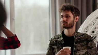 Genç sakallı bir adam elinde bir fincan kahve tutuyor ve iş arkadaşlarıyla iletişim kuruyor. Genç bir adam öğle yemeği arasında meslektaşlarıyla son haberleri tartışıyor. Yüksek kalite 4k görüntü