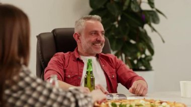 Bir grup insan bir masaya oturup pizza yemek için hazırlanıyorlar. İşçiler zor bir haftanın sonunda pizza ve alkollü içeceklerle küçük bir parti düzenlediler. Yüksek kalite 4k görüntü