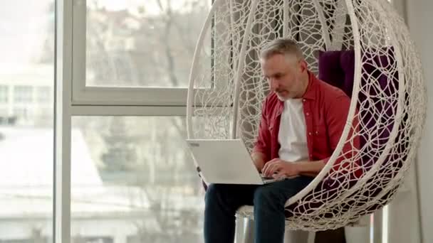 Homem Cabelos Grisalhos Senta Uma Cadeira Suspensa Digita Laptop Homem — Vídeo de Stock