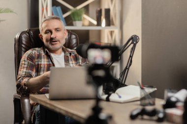 Bir erkek blogcu yeni videosu için bir giriş kaydediyor. Sakallı bir adam bir sandalyeye oturur ve masanın üzerindeki kameraya bakar. Yüksek kalite fotoğraf