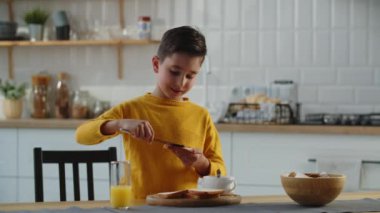 Sarı ceketli bir çocuk elinde bir dilim ekmek tutuyor ve üzerine reçel sürüyor. Aç bir çocuk kendisi için sandviç hazırlar. Yüksek kalite 4k görüntü