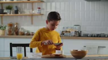 Küçük bir çocuk mutfakta kendine yabanmersinli reçelli sandviç yapıyor. Çocuk kendine bir sandviç yapar ve onu bir beslenme çantasına koyar. Yüksek kalite 4k görüntü