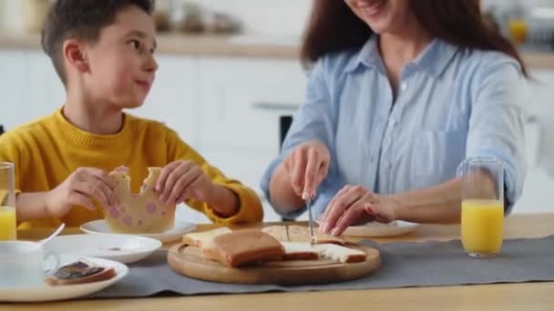 一个漂亮的黑发姑娘和她的儿子坐在厨房里为他切三明治 一个面带微笑的男孩吃着奶酪三明治 听着妈妈在告诉他一些事情 高质量的4K镜头 — 图库视频影像