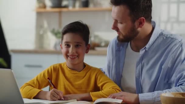 和父亲一起做作业的笑男孩 一个男人坐在他儿子旁边的桌子旁帮助他做家庭作业 高质量的4K镜头 — 图库视频影像
