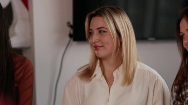 Genç bir sarışın, odanın ortasında meslektaşlarının yanında duruyor ve birini dinliyor. Ofis çalışanları toplantılarında patronlarını dinlerler. Yüksek kalite 4k görüntü