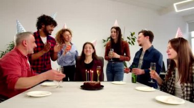 Esmer bir kadın arkadaş çemberinde masada oturur ve çikolatalı kekin üzerine mum üfler. Ofis çalışanları bir meslektaşını doğum günü için kutluyor ve şampanya içiyor. Yüksek kalite 4k görüntü