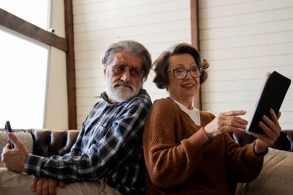 Yaşlı karı koca aktif olarak modern aletler kullanıyor. Kanepede oturan ileri büyükbaba ve büyükanne. Yüksek kalite fotoğraf