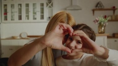Anne ve kızı eğleniyor kalp el hareketleriyle selfie çekiyorlar, gülümseyen anne küçük anaokulu kızıyla oynuyor evde kendi portresini çekiyorlar. Yüksek kalite 4k görüntü