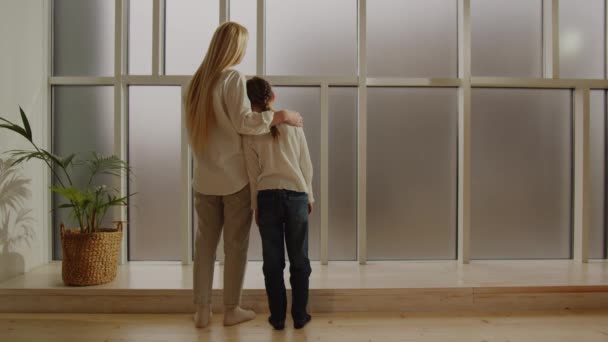 幼い母親と成長している娘が抱擁の中に立って大きな窓を見ています 母親の愛 愛情とケアのマニフェスト 高品質4K映像 — ストック動画