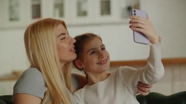 Mutlu genç anne ve tatlı küçük kız dişlek gülümsemeyle webcam 'e bakıyor. Anne ve çocuk ellerinde bir aletle akıllı telefondan kendi portresini çekiyorlar. Yüksek kalite 4k görüntü