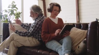Gözlüklü yaşlı çift boş zamanlarında akıllı telefon ve dijital tablet kullanıyor. Gülümseyen kıdemli adam ve kadın aletler kullanıyor. Yüksek kalite 4k görüntü