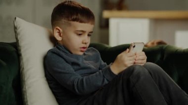 Telefonda oynayan sevimli küçük bir oğlan, arka planda eğlenen küçük bir kız. Ebeveynleri ve aletleri olmayan çocuklar. Yüksek kalite 4k görüntü