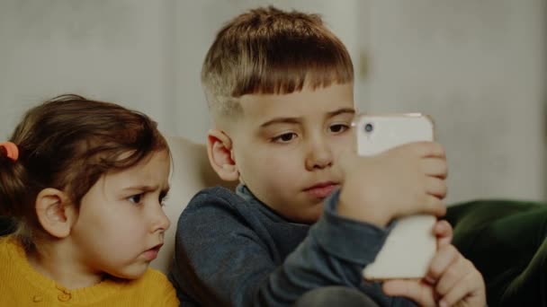 집에서 소파에 귀여운 소녀와 스위트보이는 스마트폰으로 상자를 아이들은 스마트폰을 사용하여 — 비디오