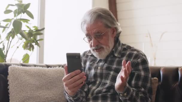 ビデオ通話中に電話画面を見ているシニア男性 眼鏡をかけた祖父と携帯電話で話しているチェックシャツ 高品質4K映像 — ストック動画