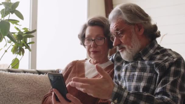 Счастливая Старшая Пара Помощью Смартфона Просматривает Интернет Вместе Сидя Диване — стоковое видео