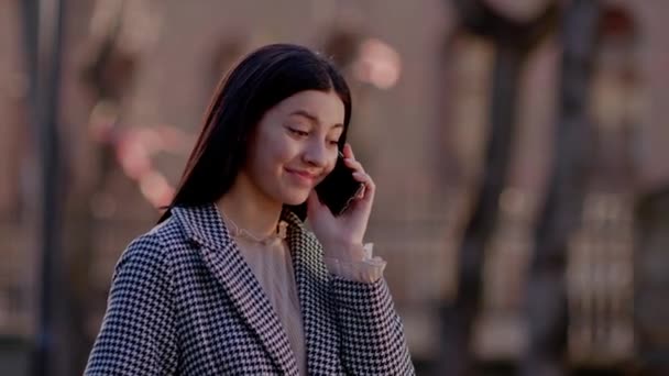 コートを着た若いブルネットの女性が電話で話して笑っている かわいい電話の会話 高品質4K映像 — ストック動画