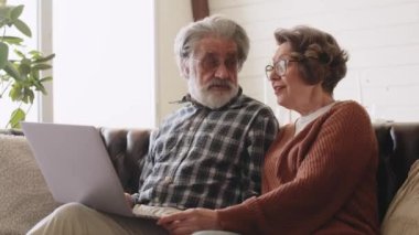 Yaşlı çift internette sörf yapmak için evdeki kanepede dizüstü bilgisayar kullanıyor. Yüksek kalite 4k görüntü