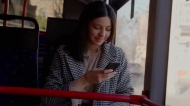 Otobüsteki çekici kız telefonu kullanıyor. Kız telefonda mesaj atıyor ve tatlı tatlı gülümsüyor. Yüksek kalite 4k görüntü