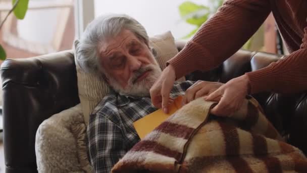 一位老人在沙发上看书时睡着了 一个有爱心的妻子用毯子盖住了他 高质量的4K镜头 — 图库视频影像