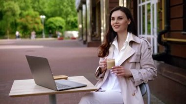 Orta yaşlı bir kadın kafede kahve içer ve dizüstü bilgisayarla çalışır. Mutlu duygular ve pahalı kaliteli kahve zevki. Yüksek kalite 4k görüntü