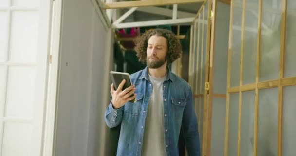 这位年轻的自由职业者在一个很长的办公室走廊里散步时使用Ipad 研究一个项目 阅读一篇文章 在网上查看邮件消息 开发一个在线应用程序 连接到4G网络 — 图库视频影像