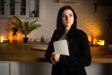 Genç esmer kadın elinde tabletle poz veriyor. Siyah kazaklı bir kadın elinde bir tablet tutuyor ve bir tarafa bakıyor. Yüksek kalite fotoğraf