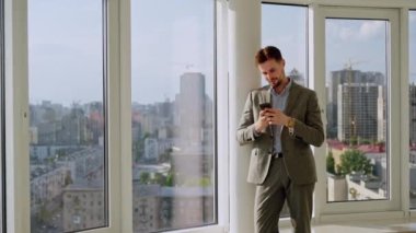 A successful young businessman in a nice suit in the office near the window picks up the phone and calls. The concept of happiness, success, and good emotions. High quality 4k footage