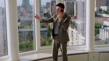 A successful young businessman in a nice suit in the office near the window picks up the phone and calls. The concept of happiness, success, and good emotions. High quality 4k footage