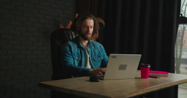 专注的白人男子在笔记本电脑上工作 而坐在一个时尚舒适的客厅里的黑色皮椅上 一个年轻的自由职业者在家里工作 浏览互联网 喝咖啡 — 图库视频影像
