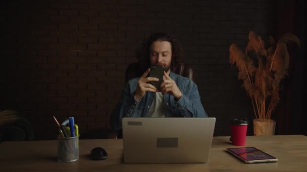 一个在办公室里留胡子的年轻自由职业者正在通过电话聊天 一个在办公室里工作了很久的孤独男人在玩电话游戏 面带微笑 高质量的4K镜头 — 图库视频影像