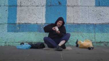 Hayatta kalmak için para isterken yardım masasında oturan evsiz, zavallı genç adam. Depresyon, sorun, kirli, sosyal, üzüntü, yalnız, umutsuzluk, sokak. Yüksek kalite 4k