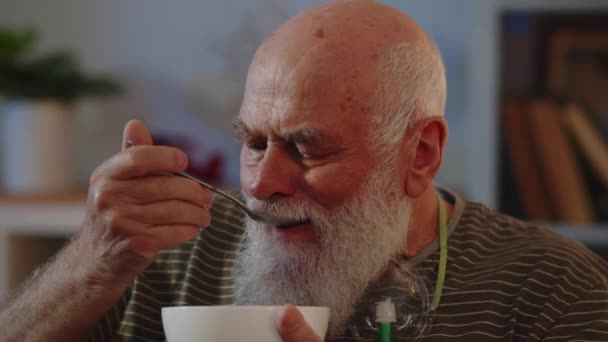 マスクを呼吸する老人は椅子に座り 食べ物を食べる 一人で夕食を家族と一緒に さまざまな肺疾患の医学的治療のテーマ 高品質の4K映像 — ストック動画