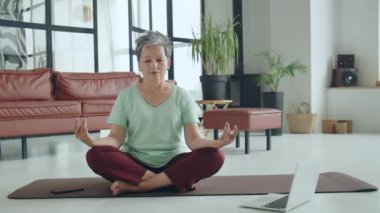 Yaşlı kadın evde yoga egzersizi yapıyor. Olgun kadın kas, boyun, eller ve kafa hareketleriyle egzersiz yapmaya hazırlanıyor. Yüksek kalite 4k görüntü