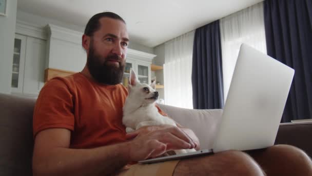 成年男子在笔记本电脑上工作 还抱着他可爱的吉娃娃小狗 男人在笔记本电脑上输入文字 小狗看屏幕 和动物在一起的快乐时刻可爱的小狗看手提电脑 高质量4K — 图库视频影像