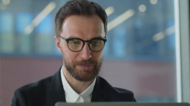 Bilgisayar ekranına bakarak online ticaret piyasasının dijital verilerini analiz eden olgunlaşmış bir işadamı. Büyük ofiste gözlüklü genç adam internette çalışıyor ve gülümsüyor.