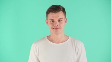 Beyaz tişörtlü genç bir adam stüdyoda mavi arka planda poz veriyor. Kendine güvenen ve yüzünde güzel bir gülümseme olan bir adam. Adam sinsi bir gülümseme ve göz kırpma sergiliyor. Gösterişli cazibe ve