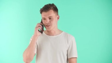 Genç mutlu adam telefonda konuşuyor. Mavi stüdyonun arka planında duruyor. Genç girişimci internet üzerinden iş organize eder, bir müşteri veya tedarikçi ile iletişim kurar. Bir erkek bir kızla iletişim kurar.