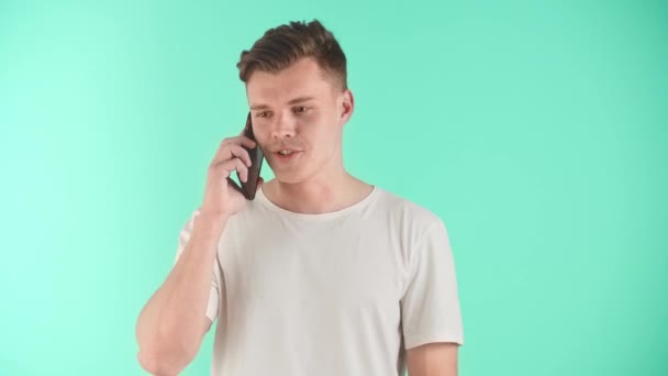 Młody Szczęśliwy Człowiek Rozmawia Przez Telefon Stojąc Nad Niebieskim Tłem — Wideo stockowe