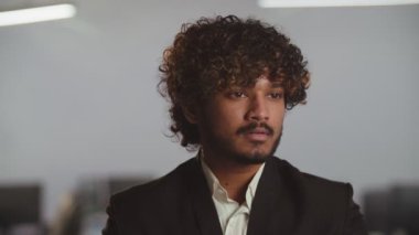 Takım elbiseli Hintli bir işadamının görüntüsü. Genç, gülümseyen bir işadamı bulanık bir ofisin önünde duruyor. Yüksek kalite 4k görüntü